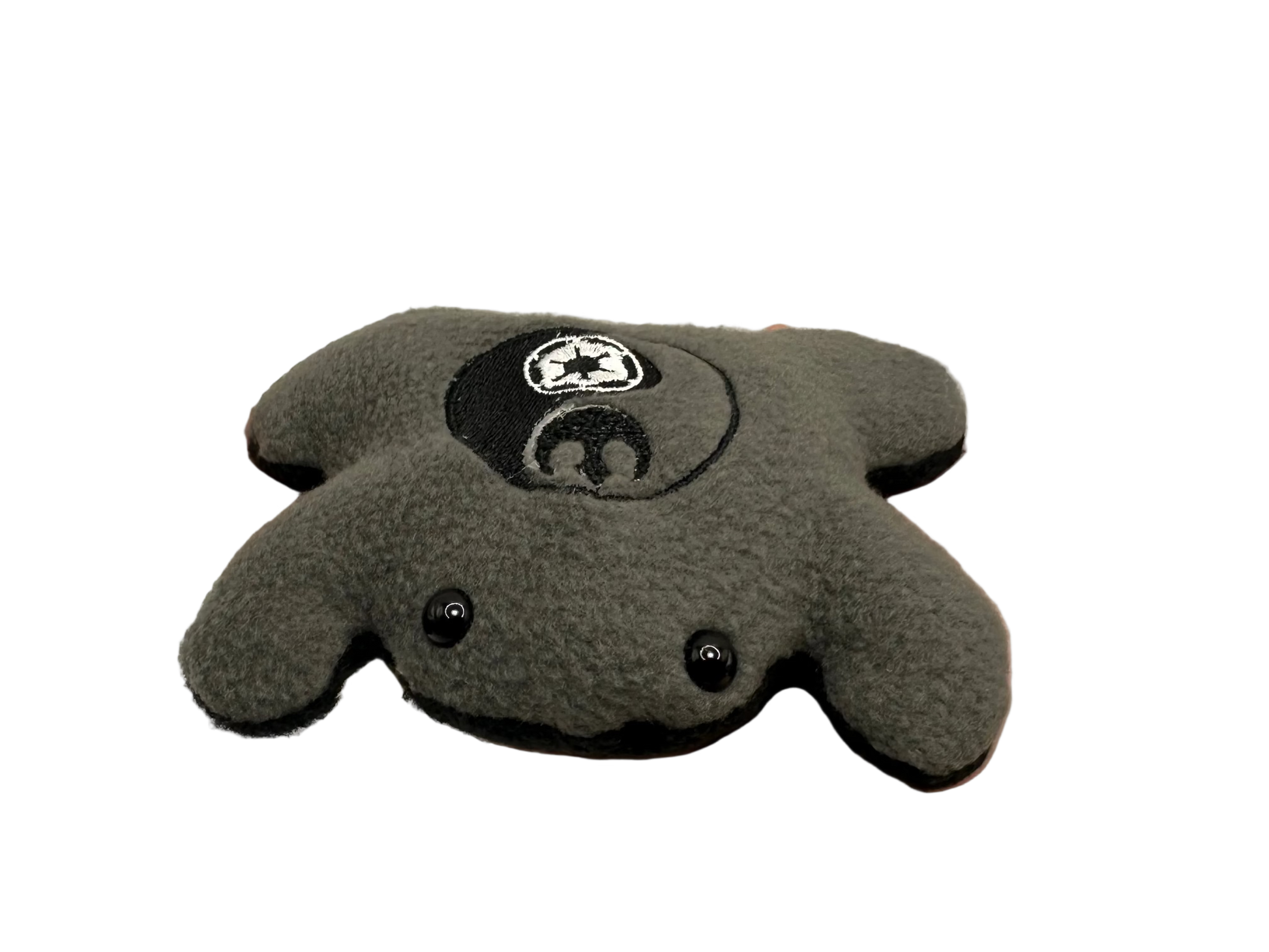Gray plush toy with a logo held in a hand against a neutral background