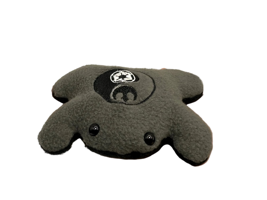 Gray plush toy with a logo held in a hand against a neutral background