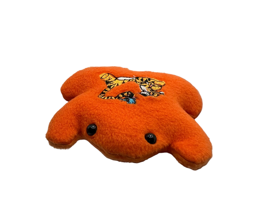 Orange plush toy with a tiger design held in a hand against a white background
